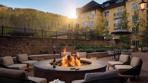 A circular outdoor seating area with a fire pit, surrounded by wicker chairs and a stone wall. - Elegant 2 bedroom condo Vail. (Vail)