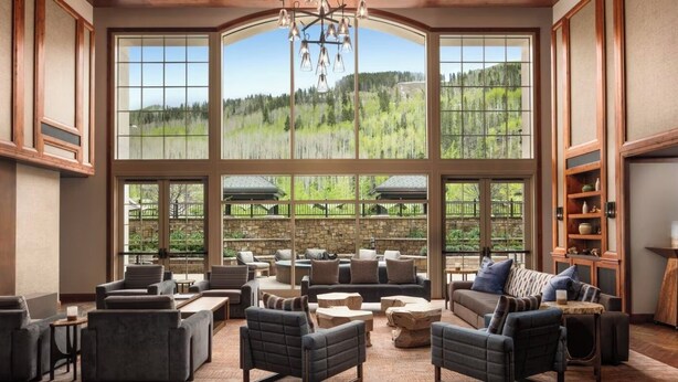 A spacious room with large windows offering a view of a forested landscape. There are multiple seating areas with sofas and chairs. - Elegant 2 bedroom condo Vail. (Vail)