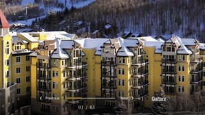 A multi-story hotel with yellow facades and a prominent red-roofed tower, set against a snowy mountainous backdrop. - Elegant 2 bedroom condo Vail. (Vail)