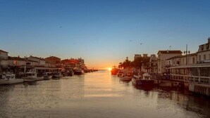 A marina with boats docked along the water's edge, buildings lining the shore, and a sunset in the background. - Coastal Comfort for Four (Le Grau-du-Roi)