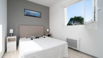 Een slaapkamer met een bed, twee nachtkastjes met lampen, een radiator, een raam met uitzicht en een lijst met een afbeelding aan de muur.