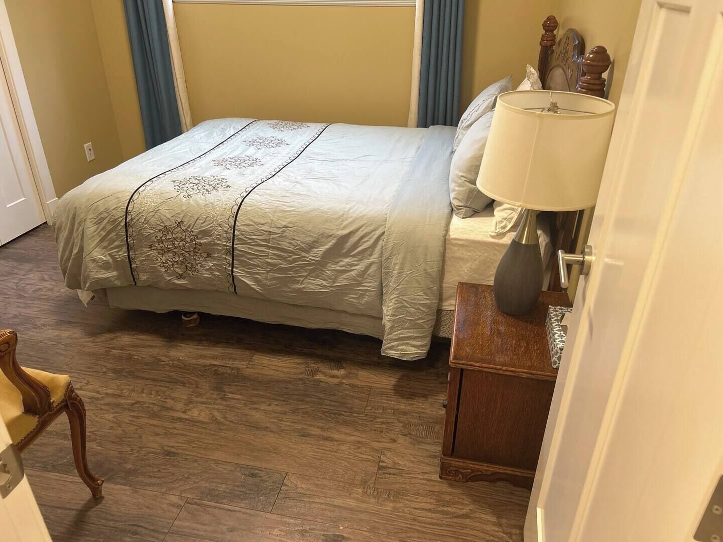 Un lit bien fait, avec une couvre-lit à motifs, une lampe de chevet et une table de chevet en bois.