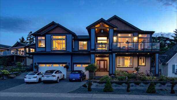 Une maison à deux étages avec un balcon, une allée permettant de garer trois voitures et un jardin bien entretenu.