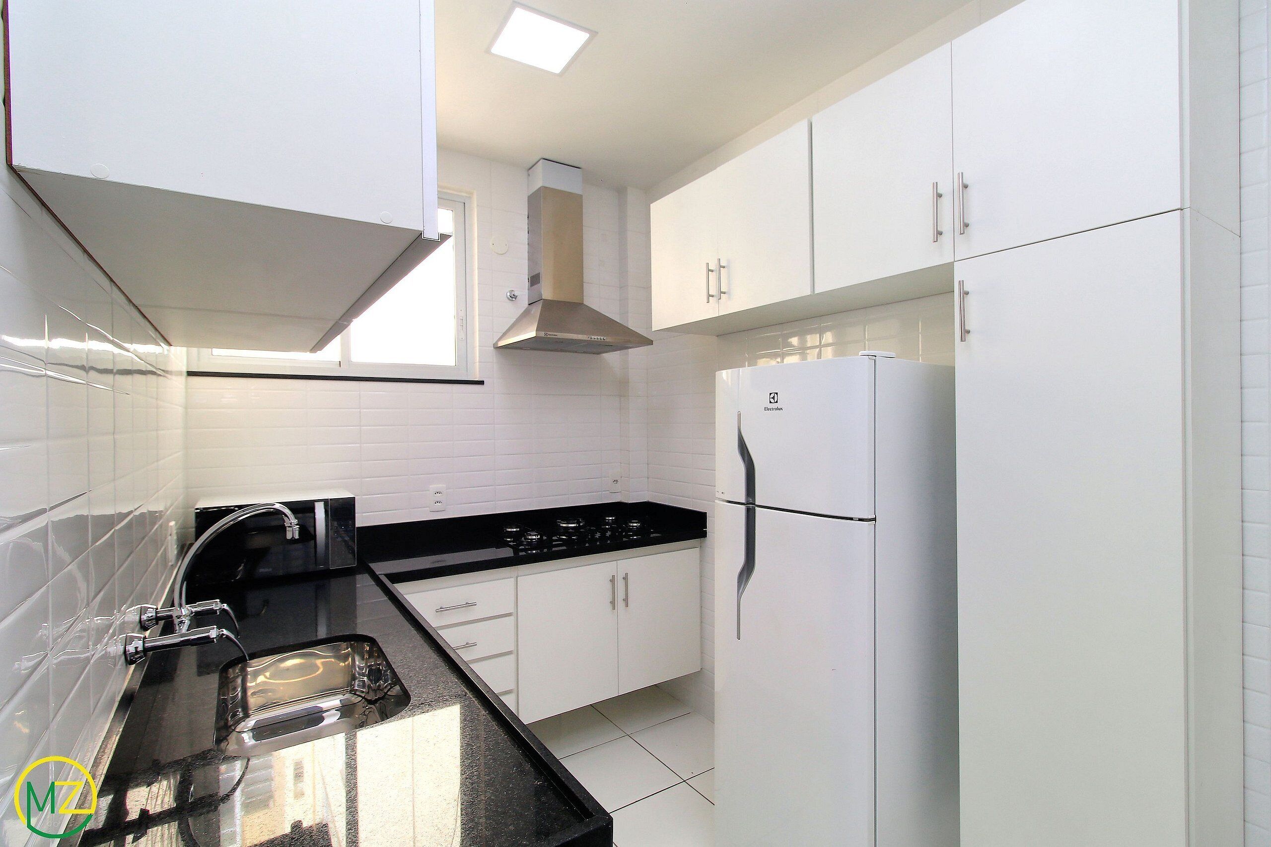 A modern kitchen with white cabinets, a black countertop, and a stainless steel range hood.