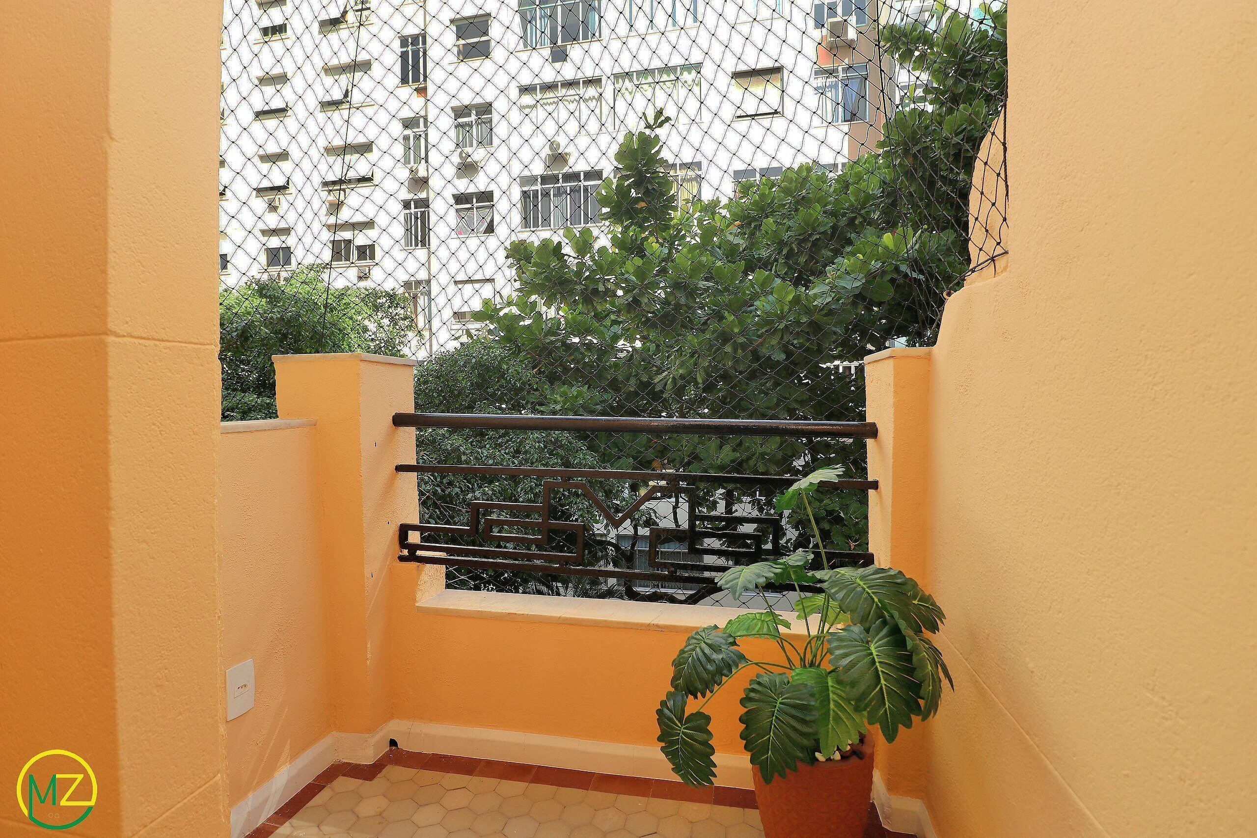 A balcony with a metal railing, a potted plant, and a view of a building with multiple windows and balconies.