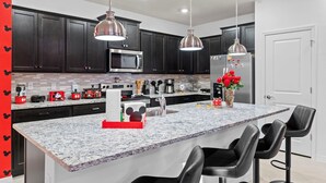 Une cuisine moderne avec des meubles de couleur sombre, des appareils en acier inoxydable et un îlot en marbre agrémenté de tabourets de bar.