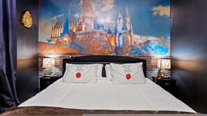 Une chambre avec une grande fresque murale représentant un château, une tête de lit noire, du linge de lit blanc et deux tables de chevet avec des lampes.