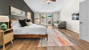 A bedroom with a bed, a ceiling fan, a nightstand, a lamp, a chair, a couch, and a door. - Twilight Tunes - Pool, Glowing Arcade Experience (Indio)