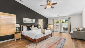 A bedroom with a bed, bedside tables, a ceiling fan, a window with blinds, and a view of the outdoors. - Twilight Tunes - Pool, Glowing Arcade Experience (Indio)