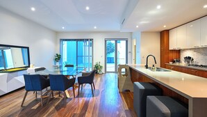 A modern kitchen with a central island, wooden cabinets, and a large window. - Cozy 3-bedroom house with Wifi/AC and only mins from cafes and perth cbd. (Subiaco)