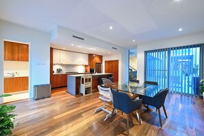 Eine moderne Küche mit Holzausbau, einer zentralen Kochinsel und einem Essbereich mit Glastisch und Stühlen.