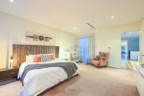Ein modernes Schlafzimmer mit einem großen Bett, einem Babybett, einem rosa Sessel und einem kleinen Tisch.