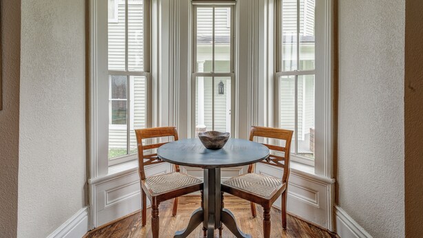 Ein Eckzimmer mit Erkerfenster, einem runden Tisch mit zwei Stühlen und einer Schüssel auf dem Tisch.