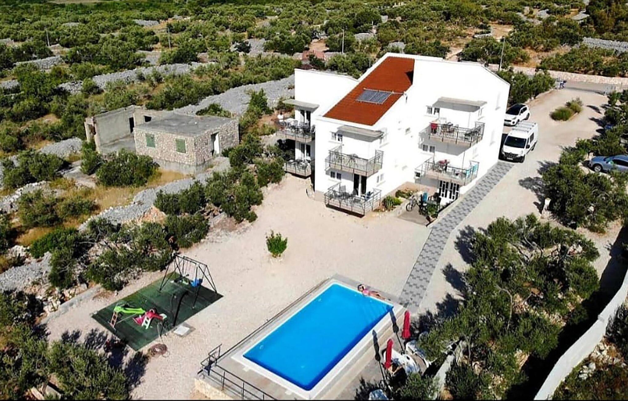 A white building with a red roof, a swimming pool, and a small garden area.