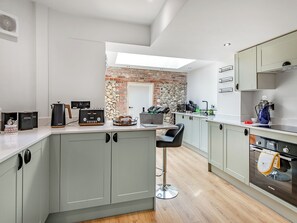 A modern kitchen with grey cabinets, a brick wall, a skylight, and a bar stool.