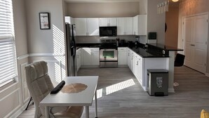 A modern kitchen with white cabinets, stainless steel appliances, and a dining area with a table and chairs.