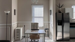 A modern kitchen with a dining area, a standing lamp, a refrigerator, and a window with blinds.