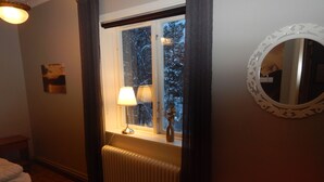 A room with a radiator, a window with curtains, a lamp, a mirror, and a painting on the wall. - Jokkmokks Vandrarhem Åsgård (Jokkmokk)