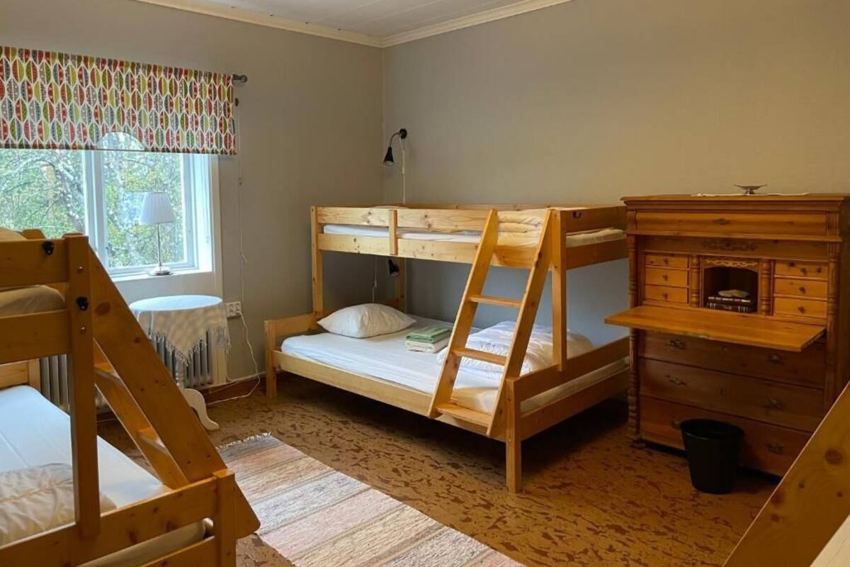 Quarto com beliche, cômoda de madeira, luminária e janela com cortinas.