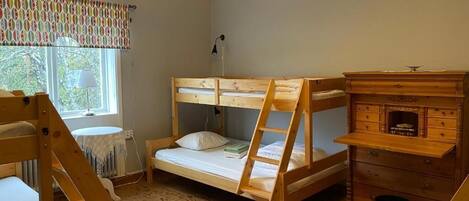 A bunk bed room with a wooden dresser, a lamp, and a window with curtains.