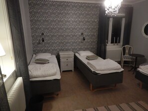 Una habitación con dos camas individuales, una mesita pequeña, una silla, un radiador y papel tapiz estampado.