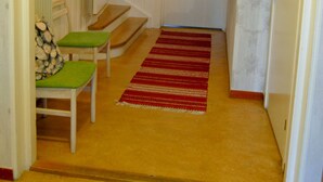 A hallway with a wooden floor, a red striped rug, a green cushioned bench, and a door with a heart decoration. - Jokkmokks Vandrarhem Åsgård (Jokkmokk)