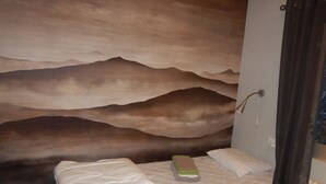 A bed with a white mattress and pillows, a green book, and a wall with a mountain landscape mural. - Jokkmokks Vandrarhem Åsgård (Jokkmokk)