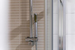 A shower with a chrome faucet and a handheld showerhead mounted on a wall. - Office Residence One (Oporto)