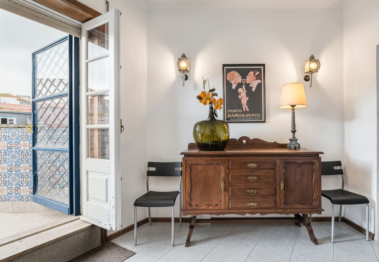 Een kamer met een houten kast, twee stoelen, een vaas met bloemen en een poster aan de muur.