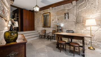 A stone-walled room with a wooden desk, chairs, and a lamp.