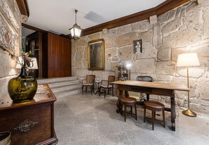 Una habitación con paredes de piedra, un escritorio de madera, sillas y una lámpara.