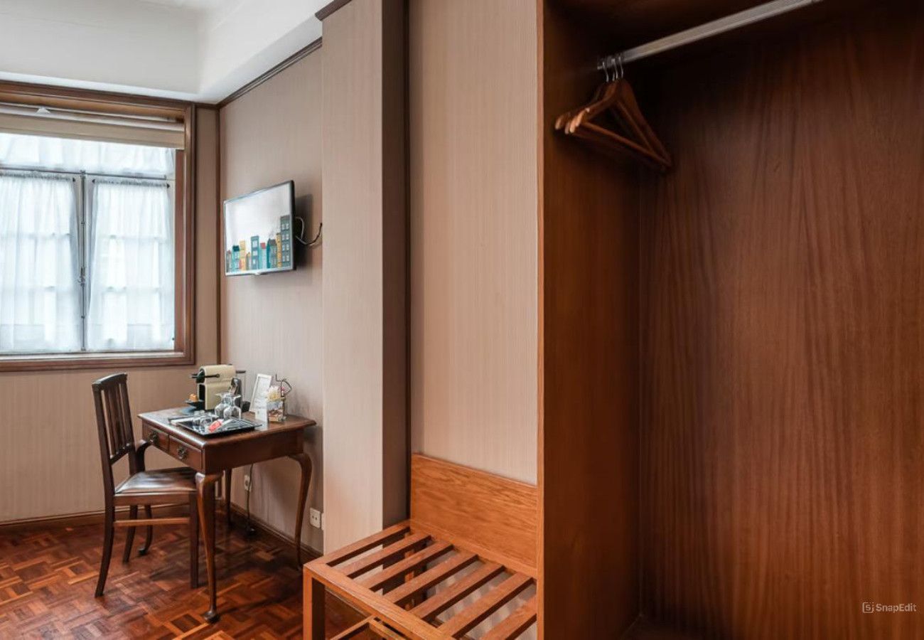 Une pièce comprenant un bureau en bois, une chaise et un banc. On y trouve également un porte-manteau et une armoire.