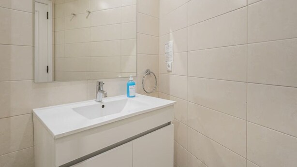 A bathroom with a white sink, mirror, and tiled walls.
