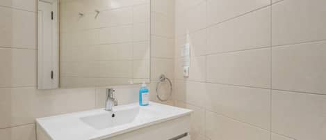 Une salle de bain avec un lavabo blanc, un miroir et des murs carrelés.