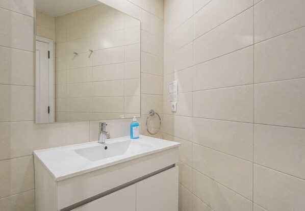 Un baño con lavamanos blanco, espejo y paredes con azulejos.