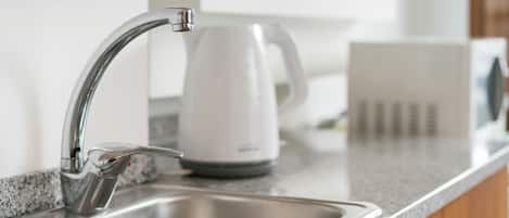 A modern kitchen with a stainless steel sink, a white kettle, and a granite countertop.