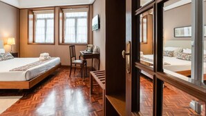 A hotel room with a wooden floor, two beds, a desk, and a chair.