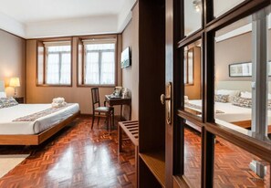 Una habitación de hotel con piso de madera, dos camas, un escritorio y una silla.