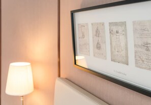 Une œuvre d’art encadrée est accrochée à un mur, et une lampe se trouve à côté.