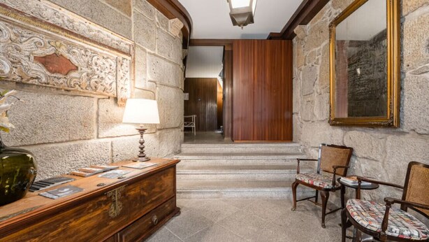 Un couloir aux murs de pierre, avec un bureau en bois, des chaises et un grand miroir.