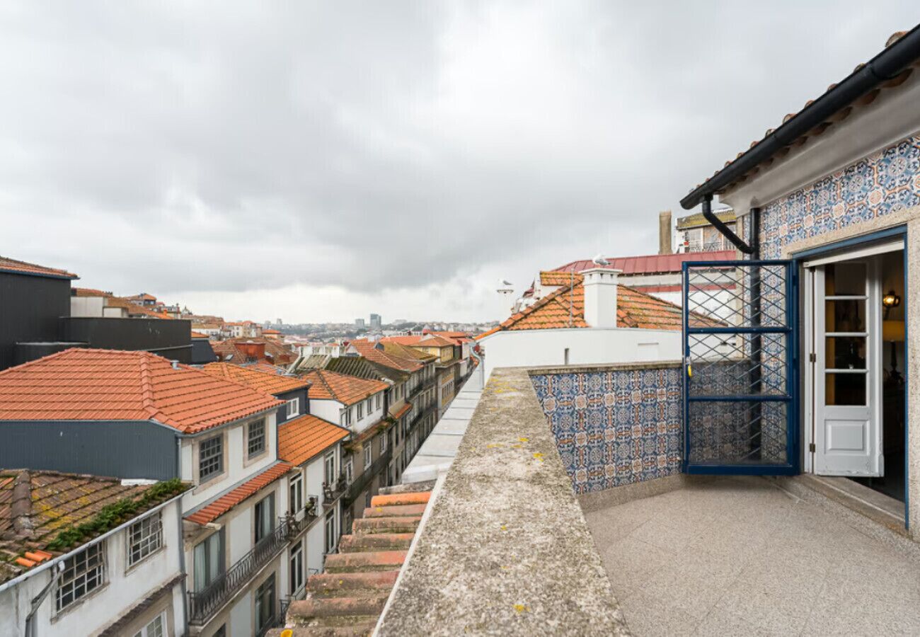 Une ruelle étroite entre deux bâtiments aux toits couverts de tuiles, un mur orné de motifs et une porte dotée d’un cadre bleu.
