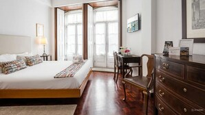 Une chambre d’hôtel avec un grand lit, un bureau et une commode. Il y a une fenêtre qui donne sur un bâtiment à l’extérieur.