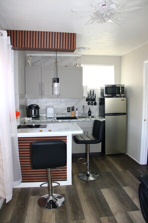 A compact kitchen with a microwave, refrigerator, and a coffee maker. There are two bar stools and a small island with a sink.