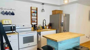 A compact kitchen with white appliances, a wooden island, and a hanging light fixture. - Highland: Driftless Fun Awaits (Highland)