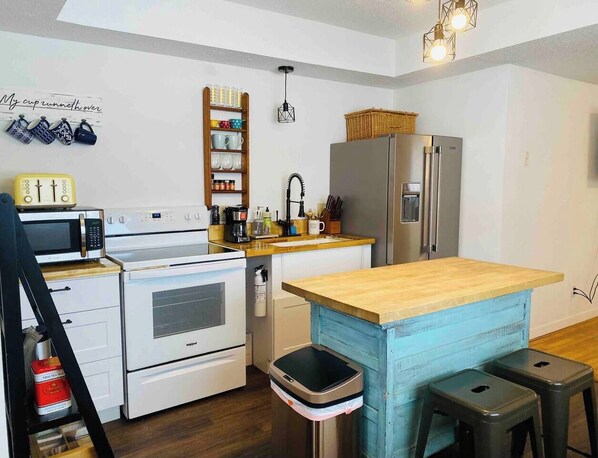 A compact kitchen with white appliances, a wooden island, and a hanging light fixture. - Highland: Driftless Fun Awaits (Highland)