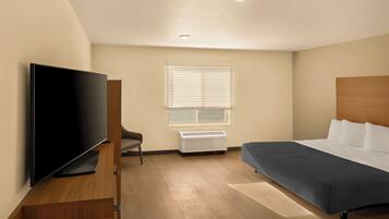 Quarto de hotel moderno com televisão de tela plana, uma cama, uma cadeira e uma janela com persianas.