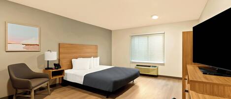 Habitación de hotel con cama, escritorio con televisor, silla, mesita de noche con lámpara y ventana con persianas.