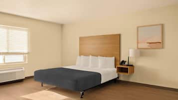 A hotel room with a large bed, a bedside table with a lamp, a painting on the wall, and a window with blinds.