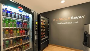 A vending machine area with Pepsi and other drinks, and a wall with the text "SNACK AWAY. Work hard. Snack hard." - LivAway Suites- Syracuse  (Syracuse)