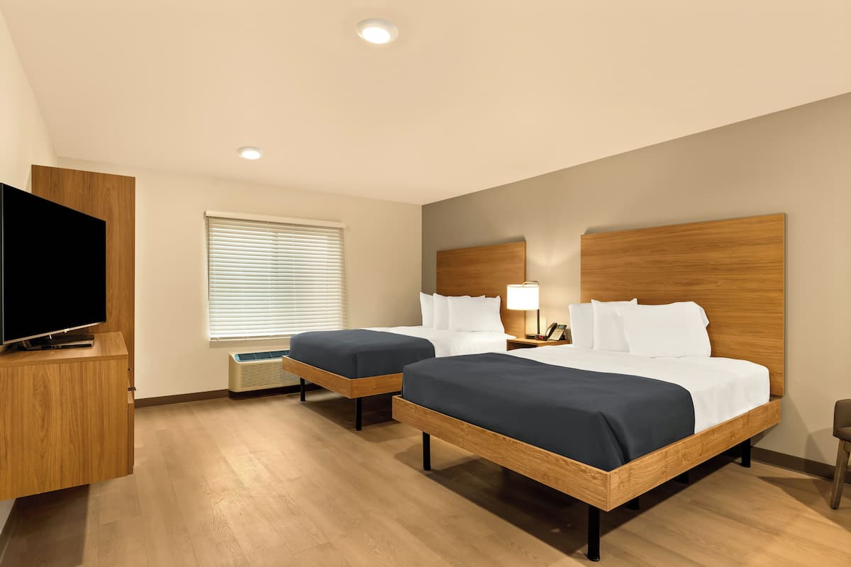 A hotel room with two beds, a TV, and a window with blinds.